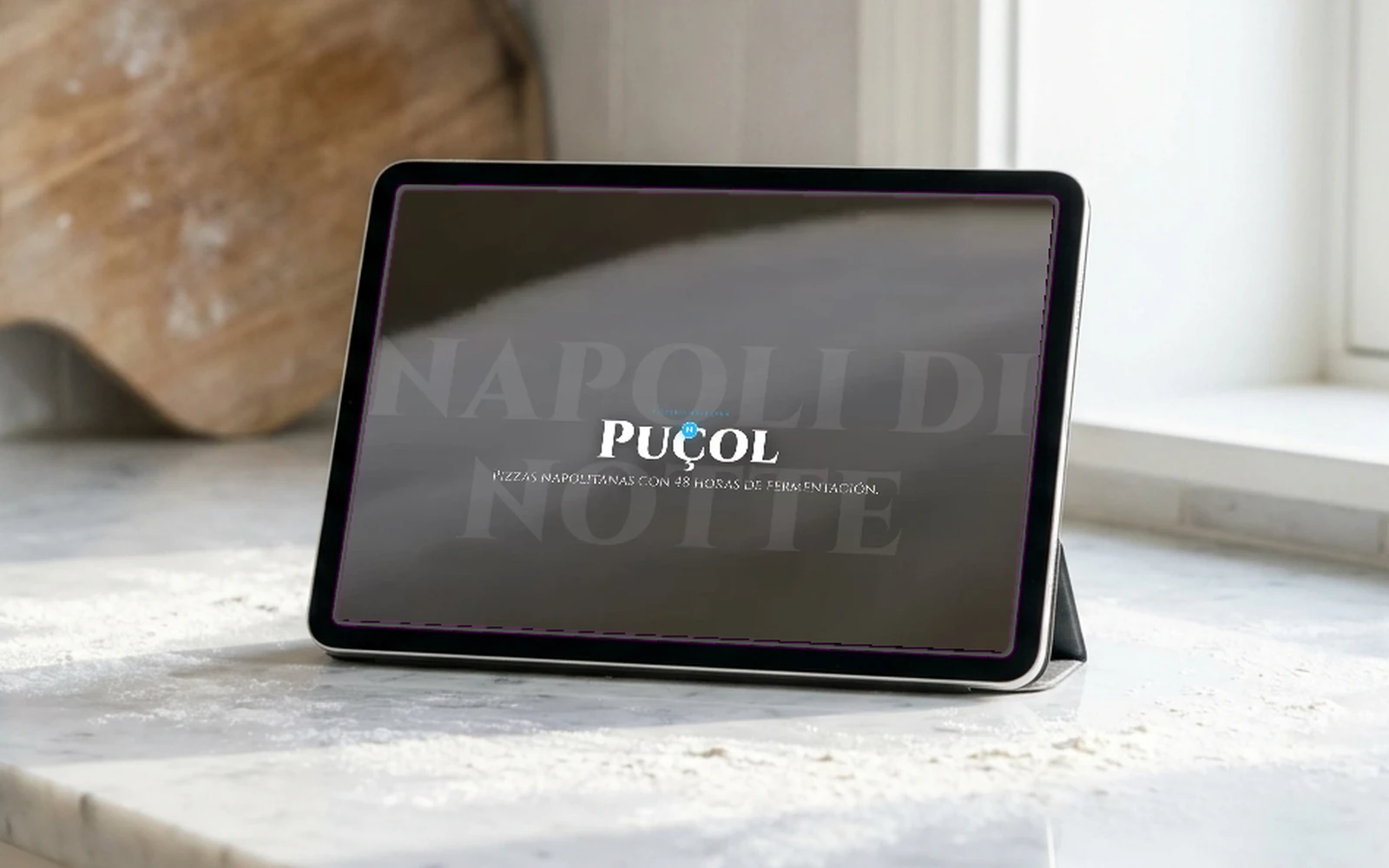 Portada de la web de Napoli Di Notte en una tablet sobre el mármol del obrador